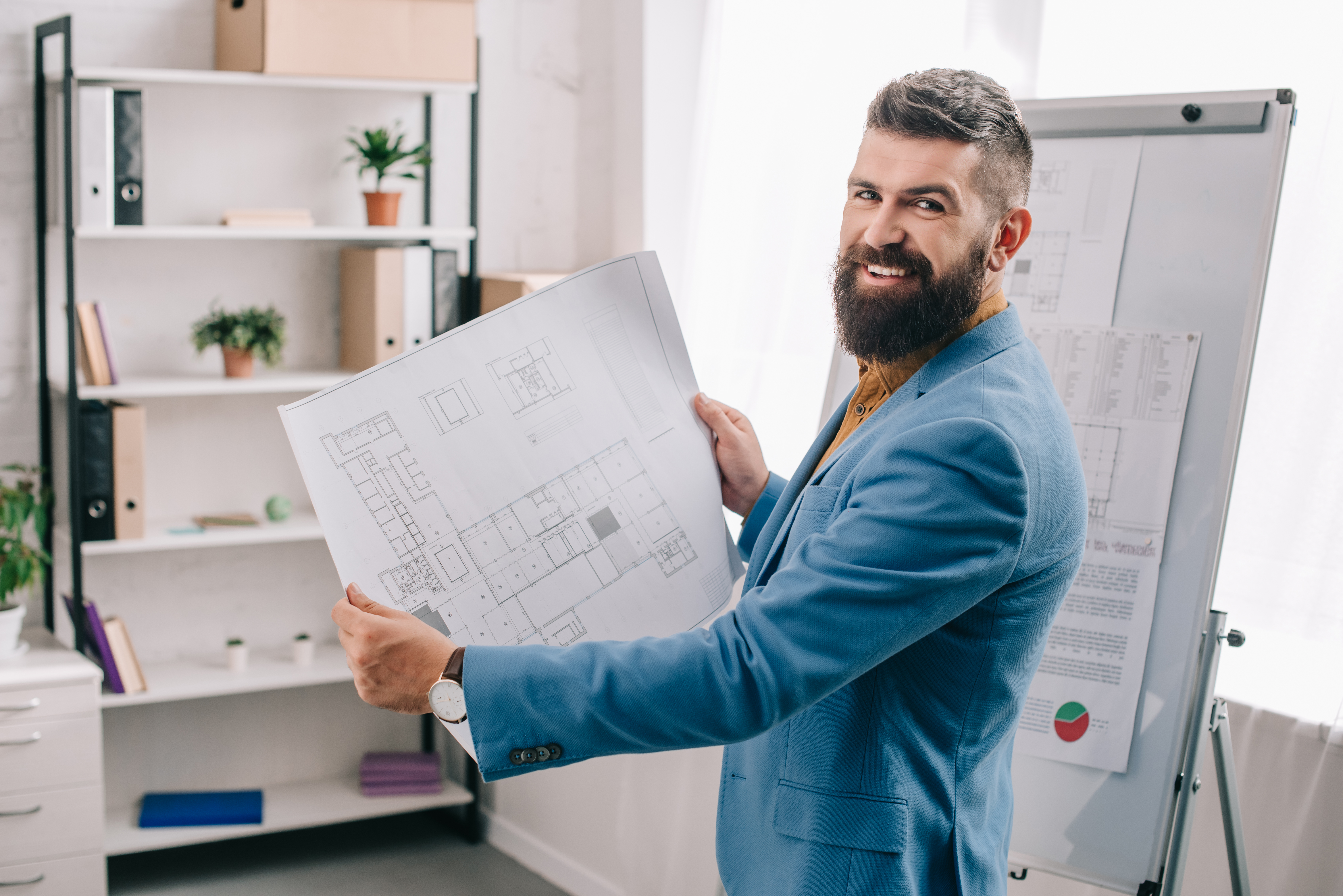 Handsome architect standing in modern office with blueprint Épületgépész Műszaki előkészítő.